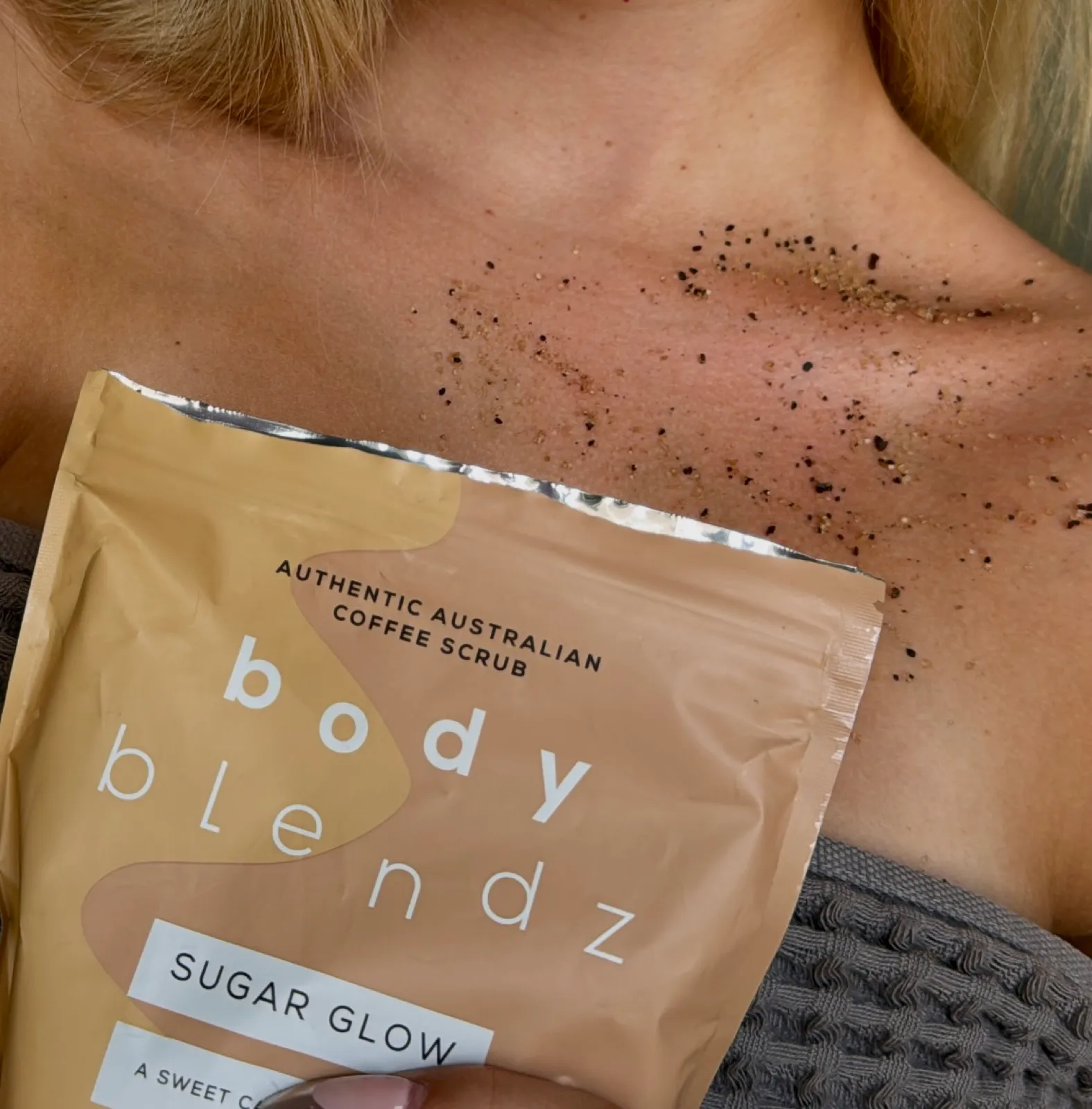 A Body Blendz coffee scrub packet held against the upper chest, with coffee scrub residue on the collarbone and chest