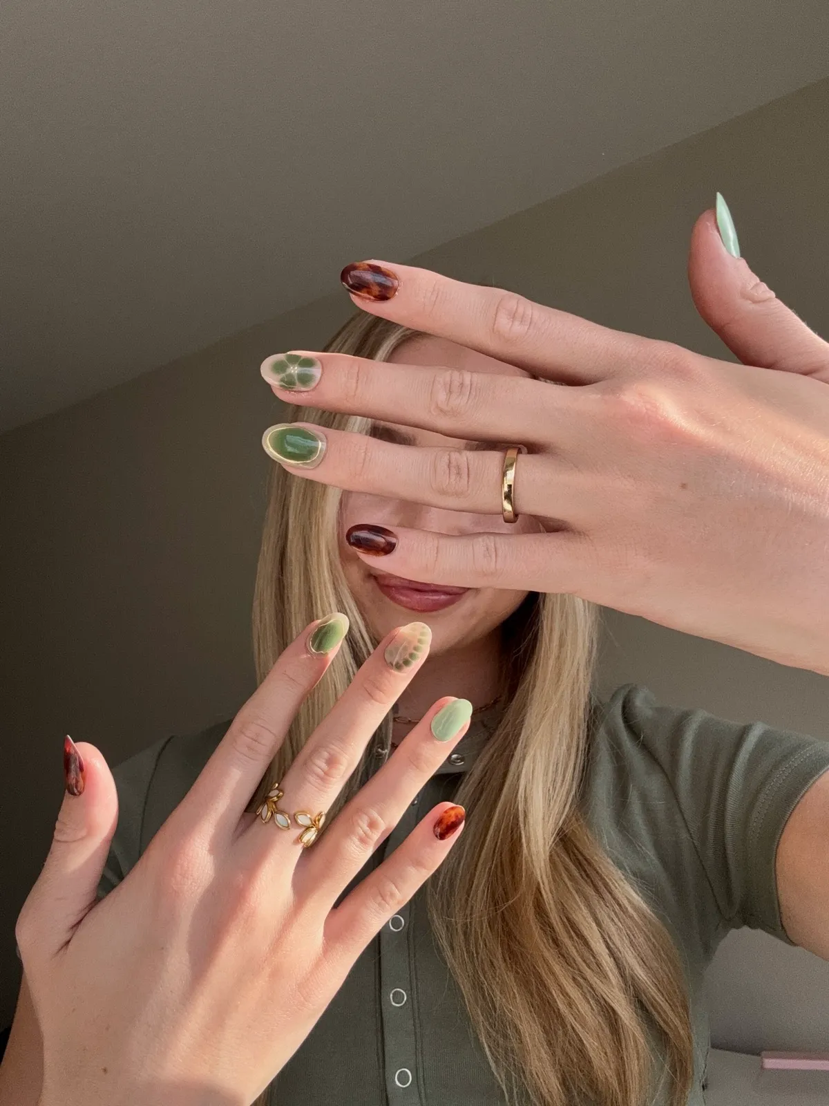 Close-up of a manicure with tortoiseshell, green and mint Dashing Diva press-on nails, hands raised over the face