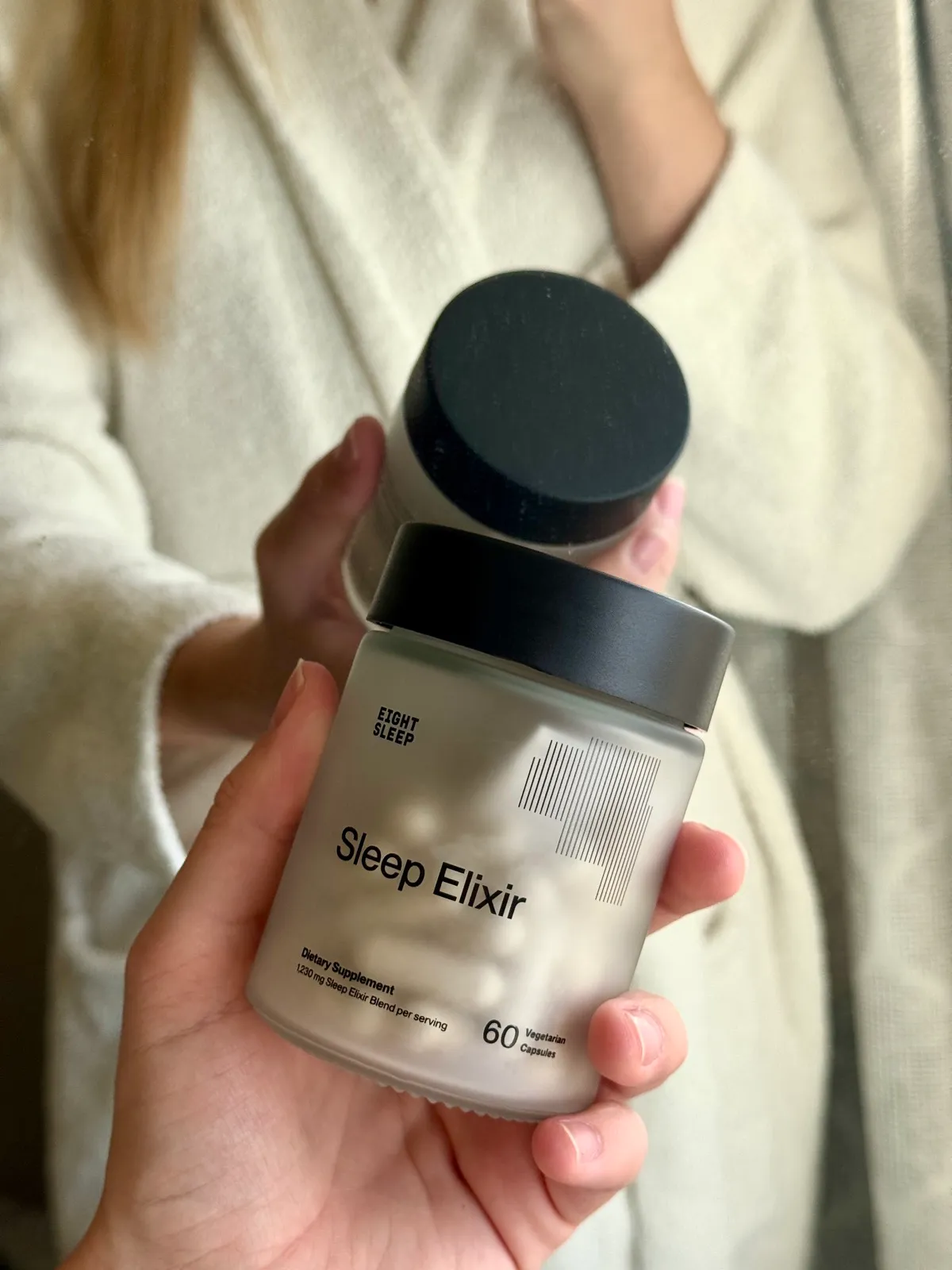 A hand holding an open jar of Eight Sleep Sleep Elixir sleep supplement capsules