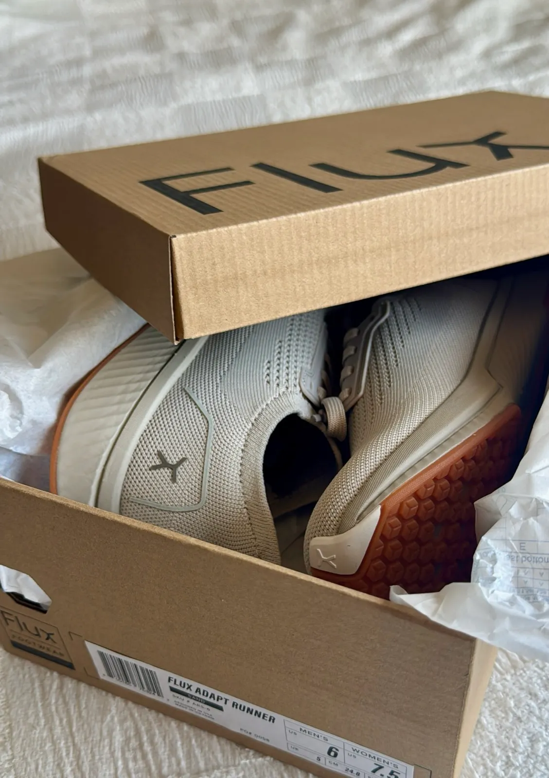 A pair of Flux Adapt Runner sneakers in their box, wrapped in tissue paper