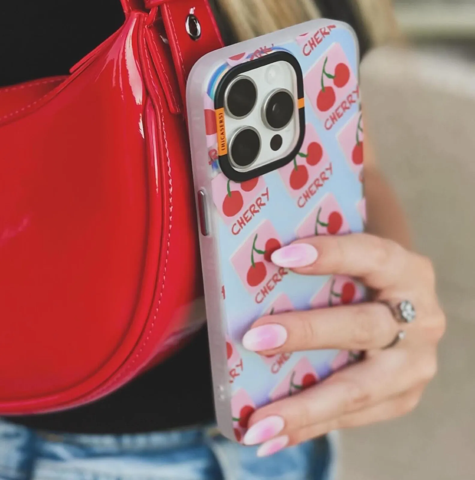 A phone in a cherry print HiCasers case held against a red patent leather bag