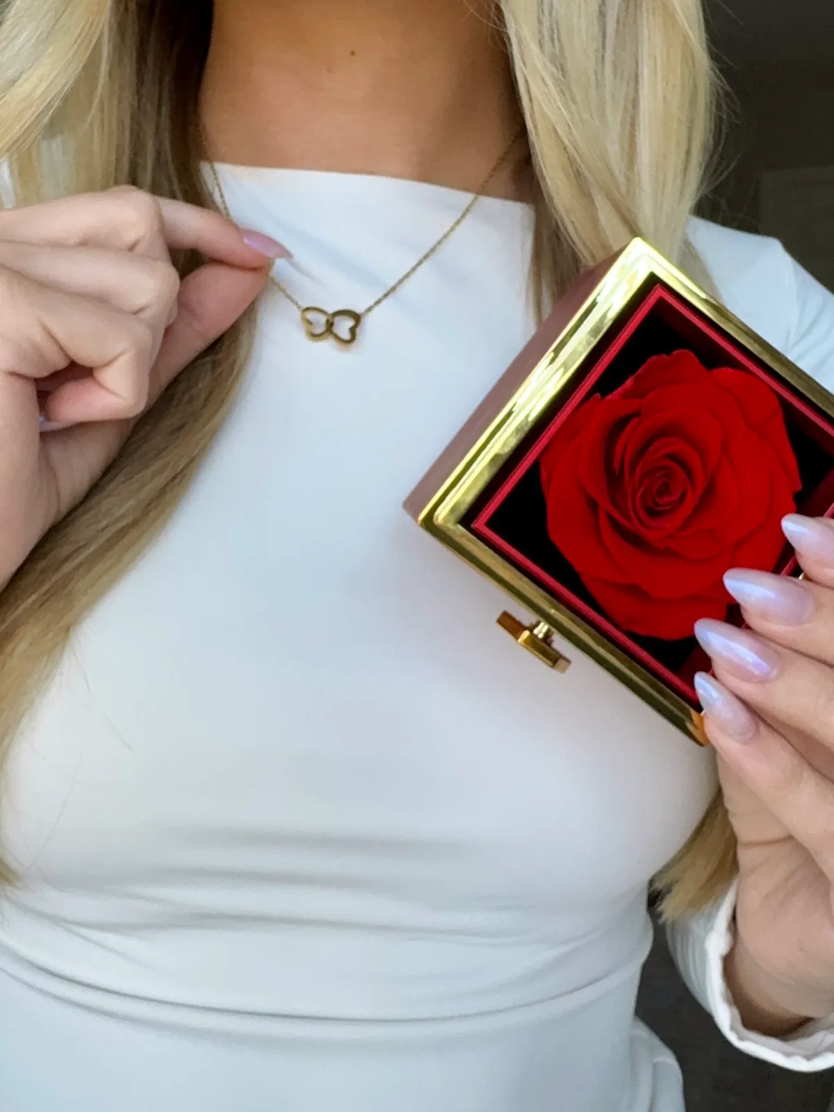 A gold butterfly necklace and an open red gift box holding a single red preserved rose